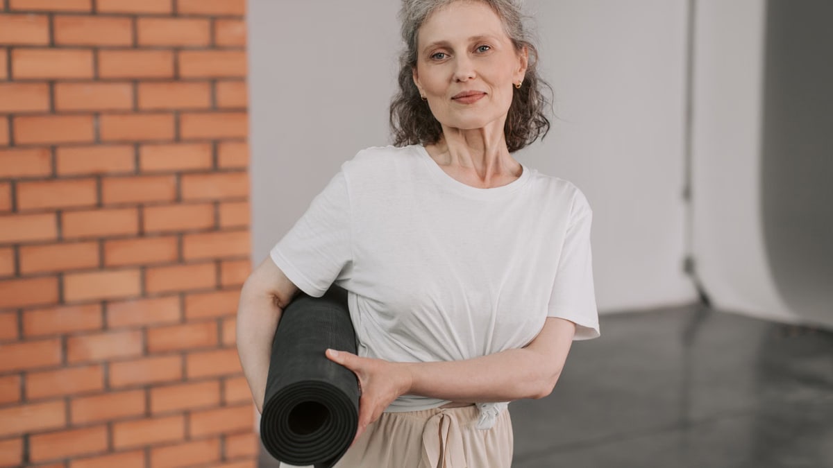 A cheerful senior woman holding a yoga mat, embracing a healthy lifestyle indoors.